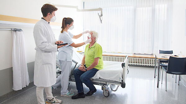 Krankenpflegerin wechselt Augenverband bei Patient daneben Arzt