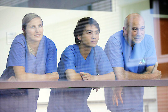 3 Krankenpflegende hinter Glasscheibe